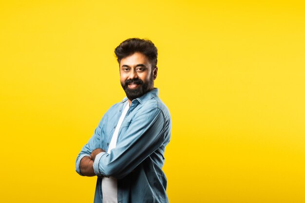 Retrato de um jovem indiano feliz barbudo com os braços cruzados em amarelo