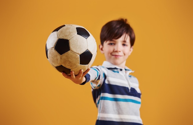 Foto retrato de um jovem jogador de futebol com uma bola em frente a um fundo amarelo