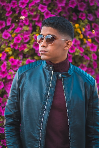 Retrato de um jovem latino com flores cor de rosa ao fundo. Jeans, jaqueta de couro e sapatos marrons