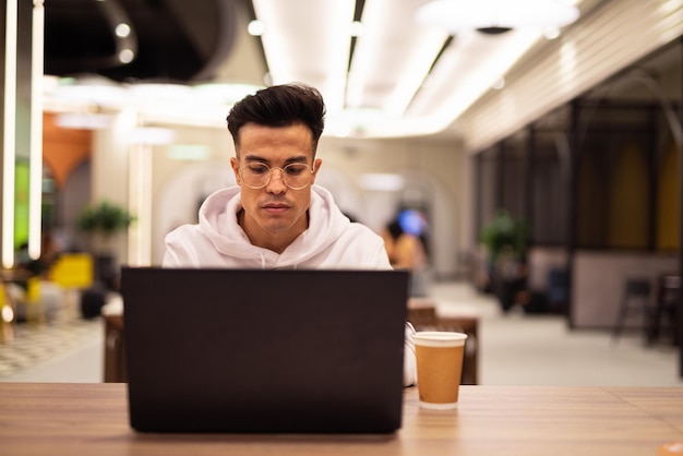 Retrato de um jovem legal bonito usando laptop no café