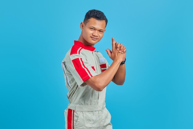 Retrato de um jovem mecânico asiático segurando uma arma simbólica com um gesto de mão sobre um fundo azul