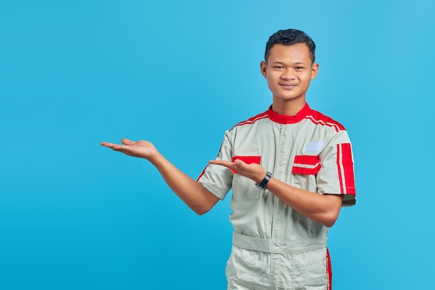 Retrato de um jovem mecânico asiático sorridente apontando para um espaço vazio isolado em um fundo azul