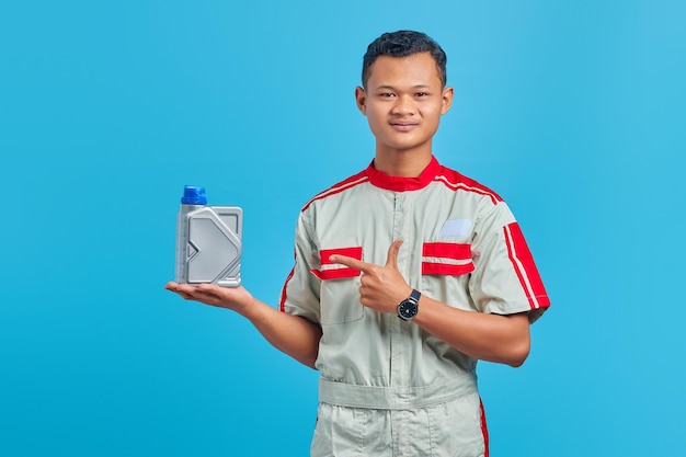 Retrato de um jovem mecânico asiático sorridente apontando para uma garrafa de plástico de óleo de motor com o dedo