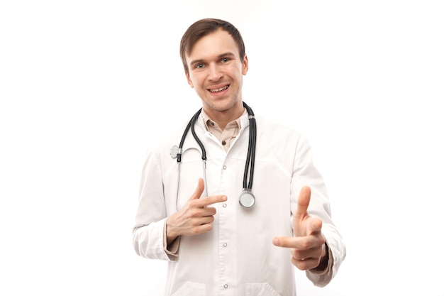 Retrato de um jovem médico amigável e positivo de jaleco branco escolhe você apontar o dedo para a câmera isolada em fundo brancoxA