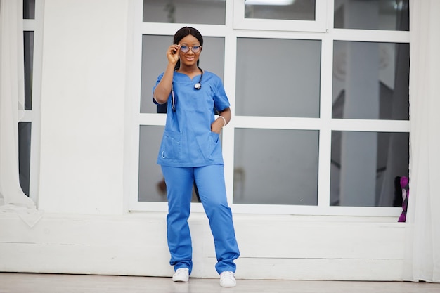 Retrato de um jovem médico pediatra americano africano feliz em casaco uniforme azul e estetoscópio contra a janela no hospital Conceito de especialista em medicina médica de saúde