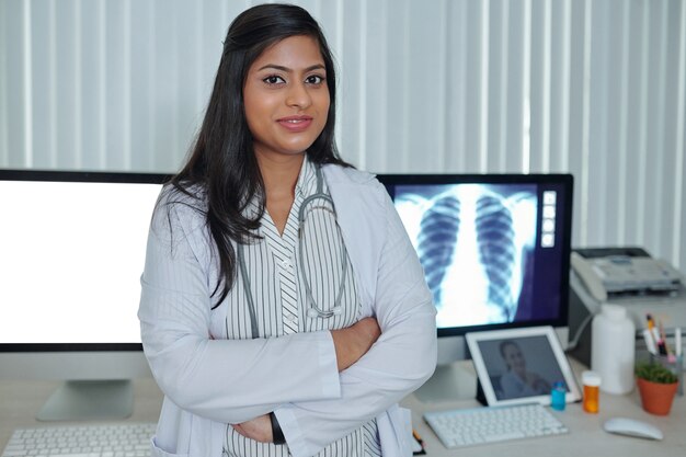 Retrato de um jovem médico sorridente e confiante em pé na mesa do escritório depois de trabalhar com uma radiografia de pulmão do paciente