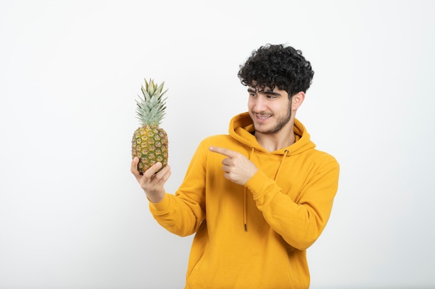 Retrato de um jovem moreno em pé e apontando para o abacaxi.