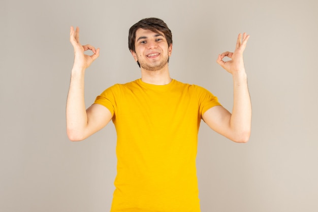 Retrato de um jovem mostrando gesto ok contra cinza.