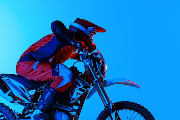 Retrato de um jovem motociclista em equipamento completo andando de moto isolado sobre o fundo azul do estúdio