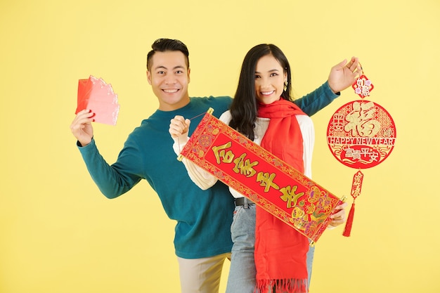 Retrato de um jovem namorado e namorada asiático sorridente, mostrando decorações chinesas com votos de inscrição para o ano que vem.