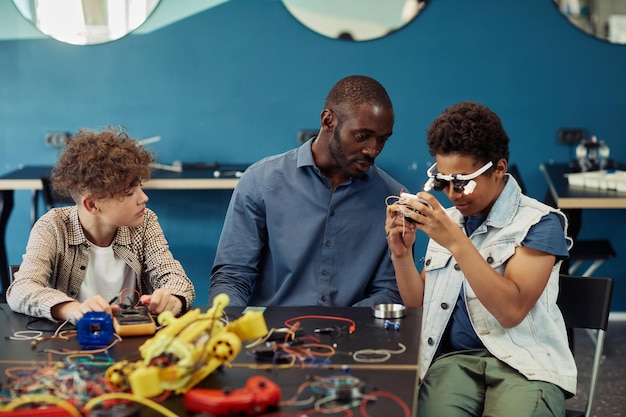 Retrato de um jovem negro construindo robôs na aula de engenharia com ajuda de professor do sexo masculino