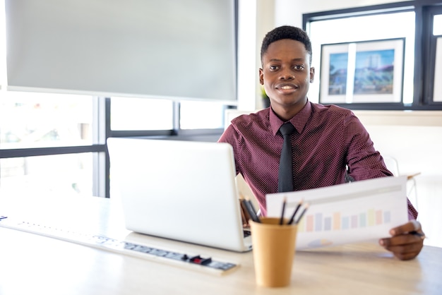 Retrato de um jovem negro usando um laptop em um ambiente de trabalho, seja um empresário africano ou um estudante.