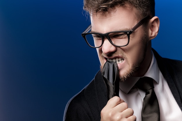 Retrato de um jovem nervoso com óculos e uma camisa branca sobre um fundo azul