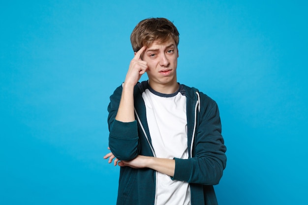 Retrato de um jovem preocupado preocupado em roupas casuais, segurando a mão perto da cabeça isolada em azul.