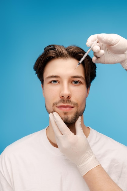 Retrato de um jovem recebendo uma injeção de beleza na testa Isolado em fundo azul Cuidados de beleza procedimentos anti-envelhecimento conceito de cirurgia plástica