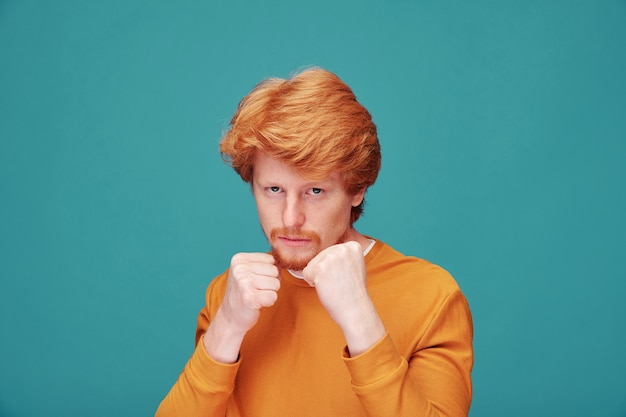 Retrato de um jovem ruivo sério com barba em pé em posição de boxe e pronto para se proteger