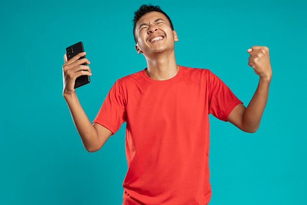 Foto retrato de um jovem satisfeito com smartphone comemorando o sucesso isolado sobre fundo azul