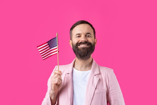 Retrato de um jovem satisfeito com uma barba com uma bandeira americana em um fundo de estúdio vermelho Grande patriota dos EUA e defensor da liberdade