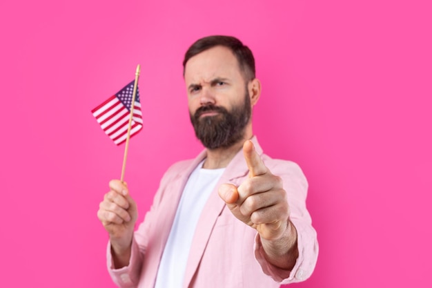 Retrato de um jovem satisfeito com uma barba com uma bandeira americana em um fundo de estúdio vermelho Grande patriota dos EUA e defensor da liberdade