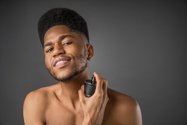 Foto retrato de um jovem sem camisa de pé sobre um fundo cinzento e usando perfumes