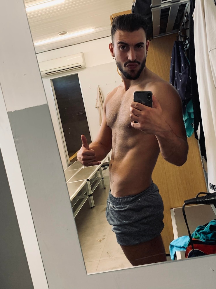 Foto retrato de um jovem sem camisa tirando uma selfie com um telefone celular refletindo-se no espelho