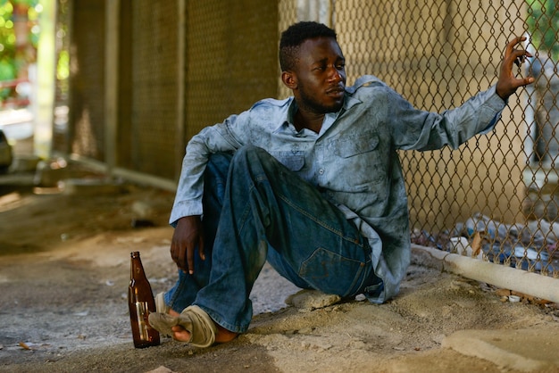Retrato de um jovem sem-teto africano contra uma cerca de arame na rua ao ar livre