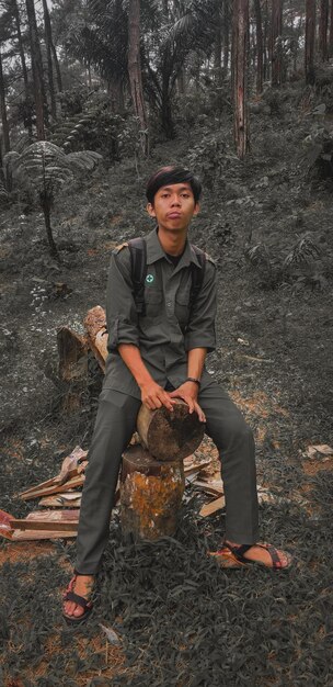 Foto retrato de um jovem sentado em terra na floresta