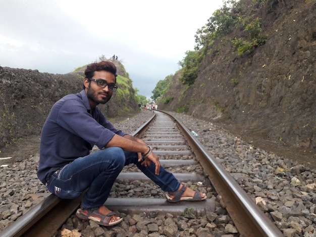Foto retrato de um jovem sentado em um trilho ferroviário em meio a uma formação rochosa