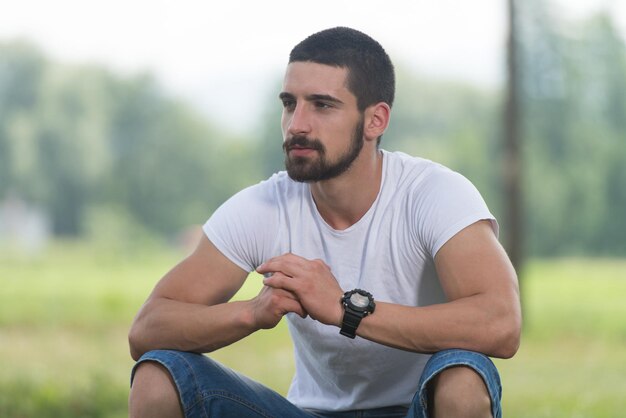 Retrato de um jovem sentado na grama, homem bonito, repouso na natureza ao ar livre