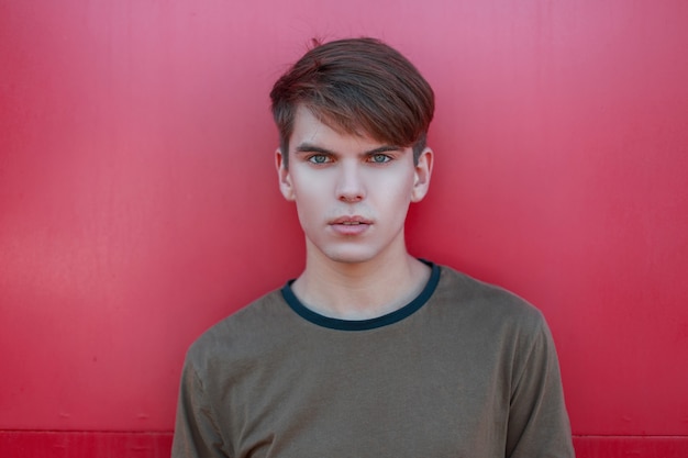 Retrato de um jovem sexy sério com um penteado elegante com pele fresca e olhos azuis em uma elegante camiseta verde de verão sobre um fundo rosa brilhante no estúdio