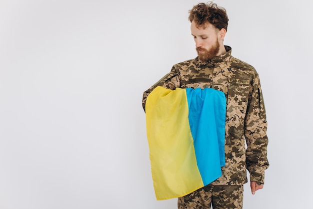 Retrato de um jovem soldado patriota ucraniano barbudo emocional em uniforme militar segurando uma bandeira no escritório