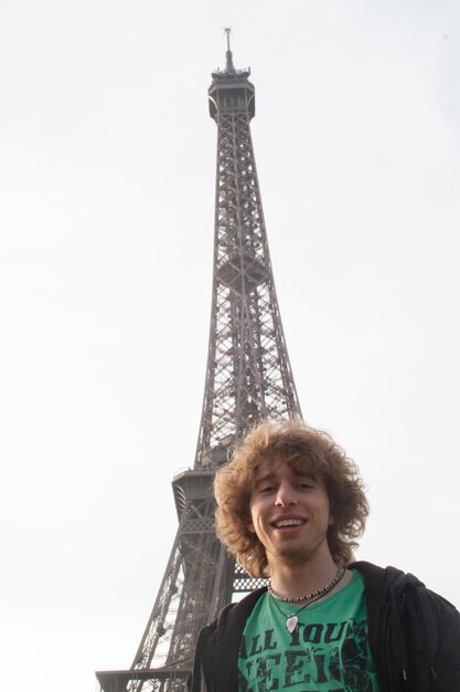 Foto retrato de um jovem sorridente contra a torre eiffel