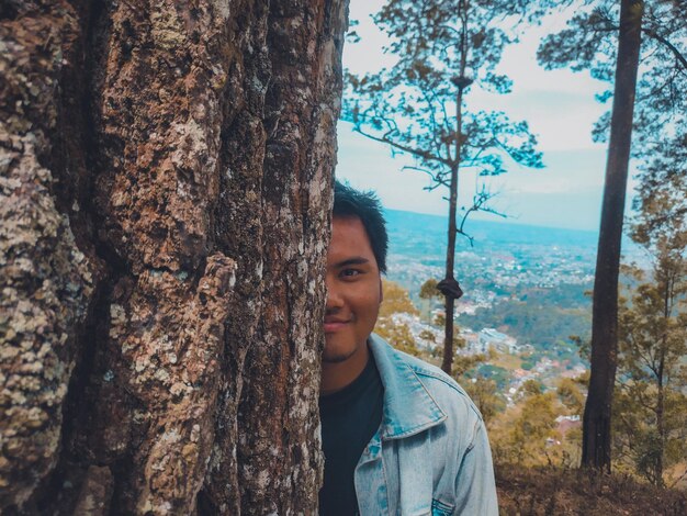 Foto retrato de um jovem sorridente no tronco de uma árvore na floresta