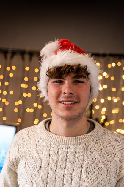 Retrato de um jovem sorridente vestindo um chapéu vermelho em frente a uma parede de luzes de Natal