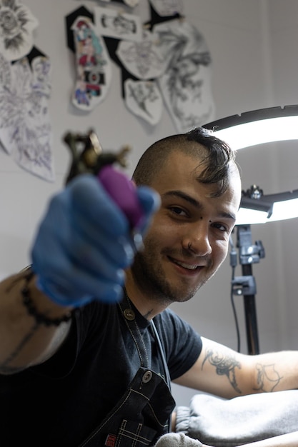 Retrato de um jovem tatuador com uma crista trabalhando em seu estúdio de tatuagem olhando para a câmera e sorrindo