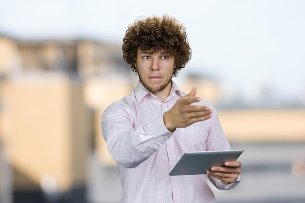 Retrato de um jovem trabalhador caucasiano com cabelos encaracolados de pé com um dispositivo de tablet PC apontando para algo