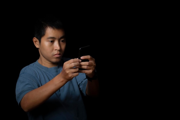 Retrato de um jovem vestindo camiseta azul usando smartphone no espaço de cópia de fundo preto