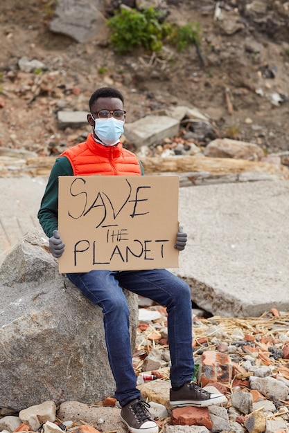 Retrato de um jovem voluntário africano sentado na pedra segurando um cartaz ao ar livre