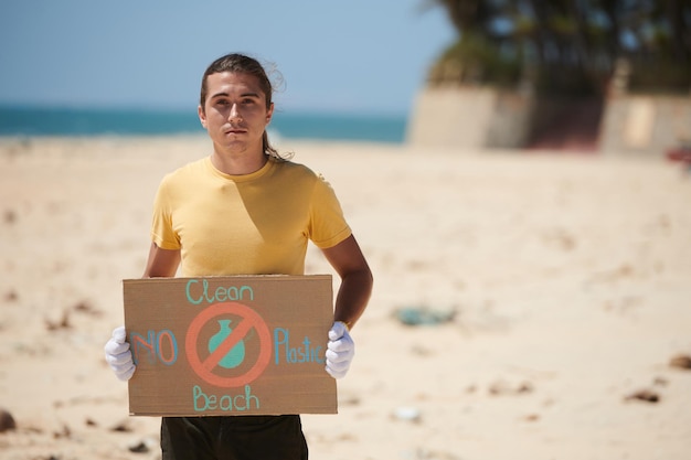 Retrato de um jovem voluntário sério segurando a praia limpa do cartaz ambiental
