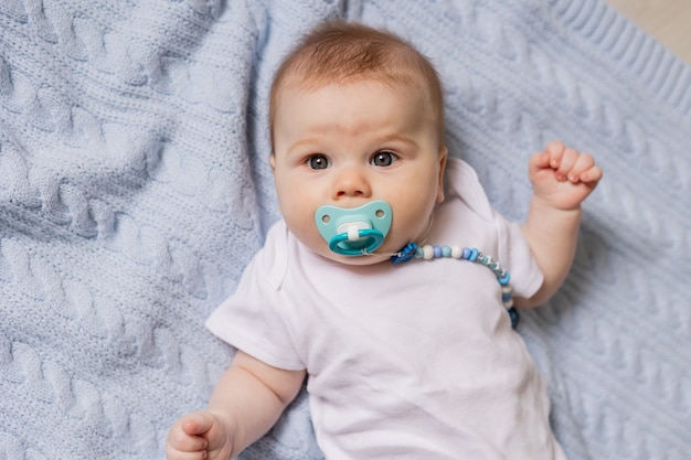 Foto retrato de um lindo bebê recém-nascido com uma chupeta na boca, deitado de costas sobre um cobertor de malha azul