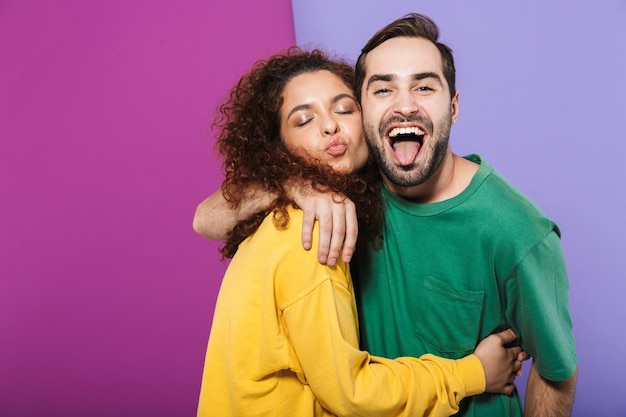 Retrato de um lindo casal caucasiano, homem e mulher com roupas coloridas, se divertindo e se abraçando isolados