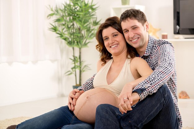 Retrato de um lindo casal jovem abraçando a barriga de grávida da mulher. Eles sorrindo e olhando para a câmera.