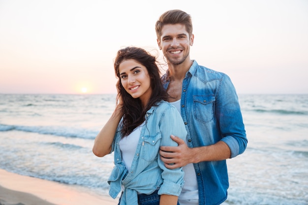 Retrato de um lindo casal jovem em pé e sorrindo na praia