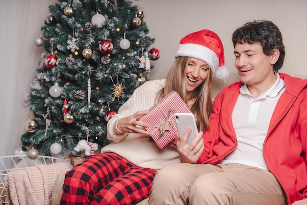 Retrato de um lindo casal, marido e mulher, com telefone celular com chapéu de Papai Noel vermelho, fazendo uma videochamada