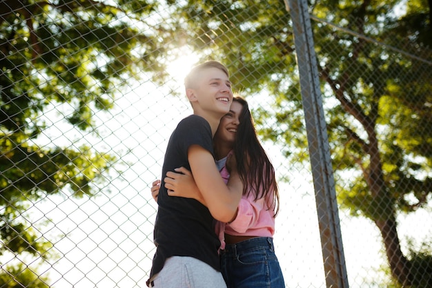 Retrato de um lindo casal sorridente em pé e abraçando um ao outro enquanto alegremente olhando de lado no parque
