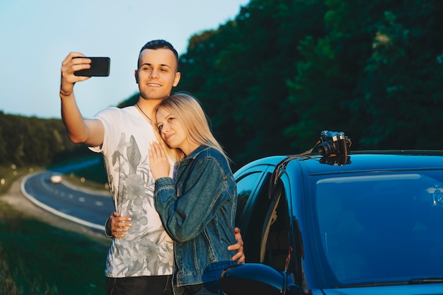 Retrato de um lindo casal tirando uma selfie se abraçando perto do carro enquanto descansava perto da estrada enquanto viajava de carro.