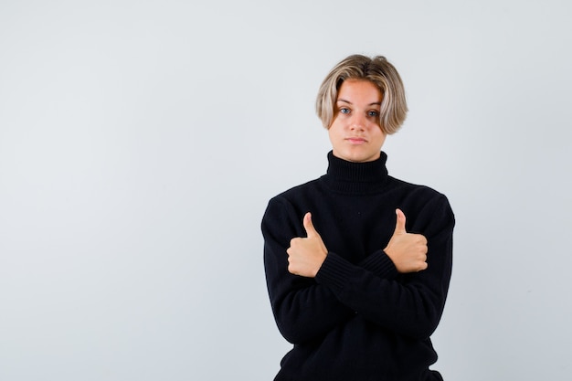 Retrato de um lindo menino adolescente mostrando dois polegares para cima com uma blusa de gola alta preta e parecendo confiante com a vista frontal