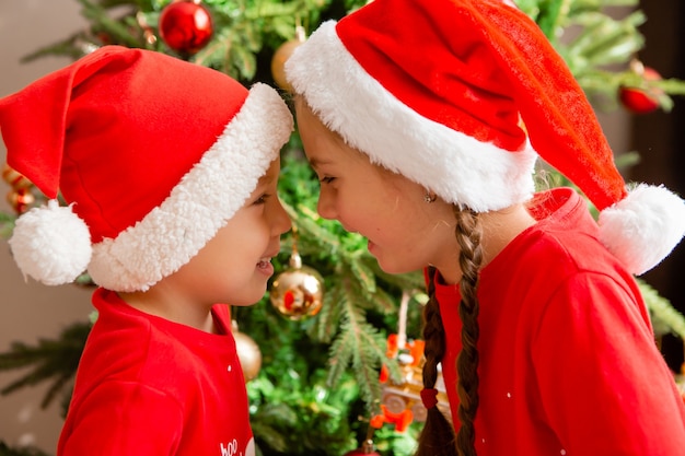 retrato de um lindo menino e uma menina de pijama vermelho no fundo de uma árvore de Natal no inverno