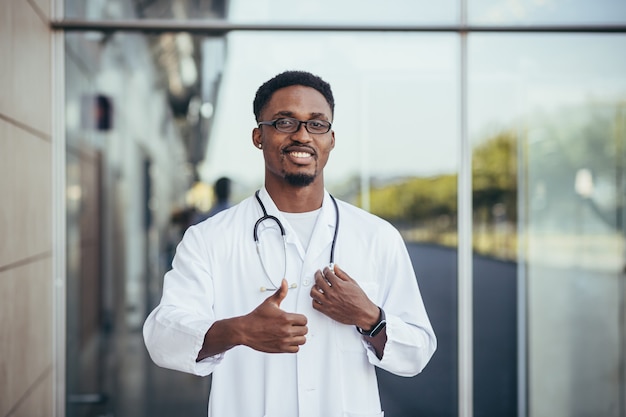 Retrato de um médico africano olhando para a câmera e sorrindo em frente à clínica