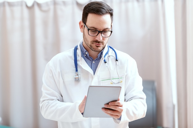 Retrato de um médico caucasiano de uniforme e estetoscópio em volta do pescoço usando o tablet. Novas tecnologias em medicina.